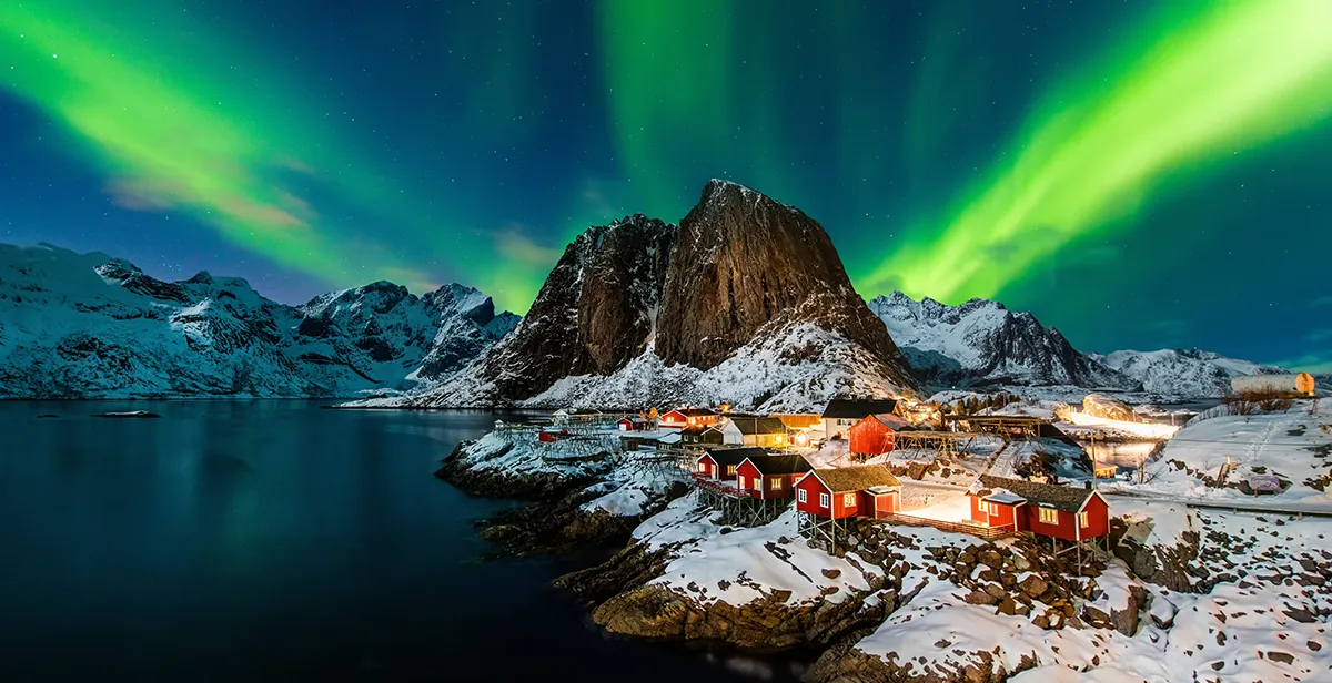 Northern lights over Arctic Norway coastline with colourful fishing village and snowy mountains