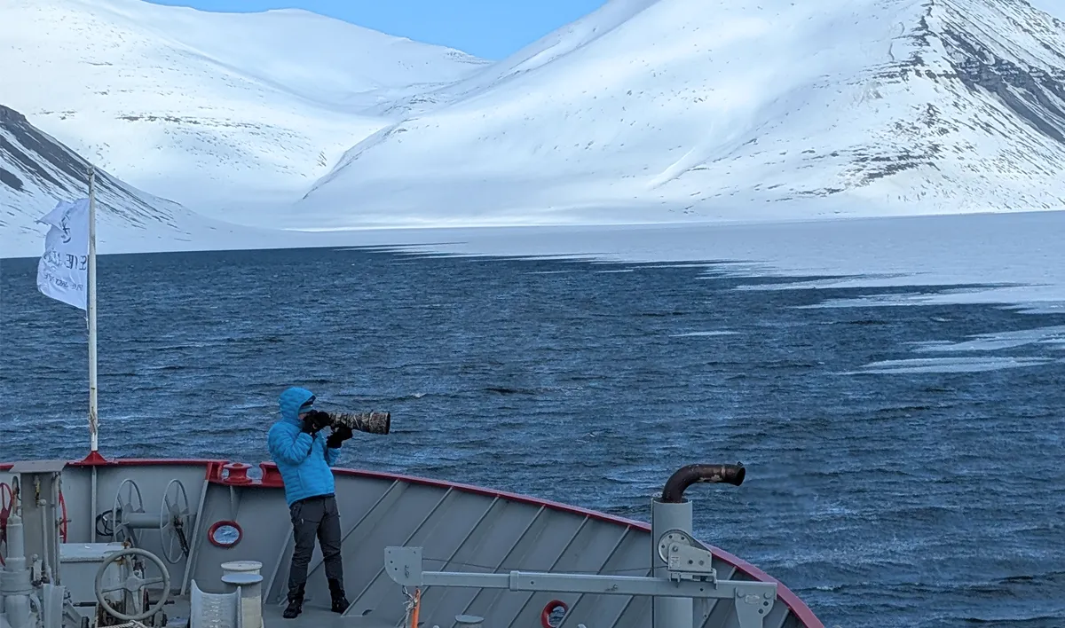 Photographer on deck of Vikingfjord expedition vessel capturing Arctic seascape and snowy mountains