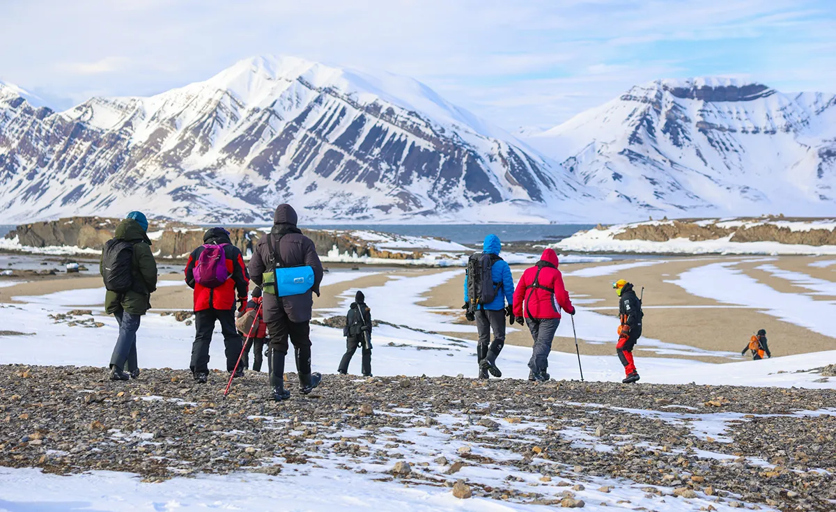 Small group of expedition participants walking on Arctic shore with snowy mountains during a Vikingfjord charter adventure