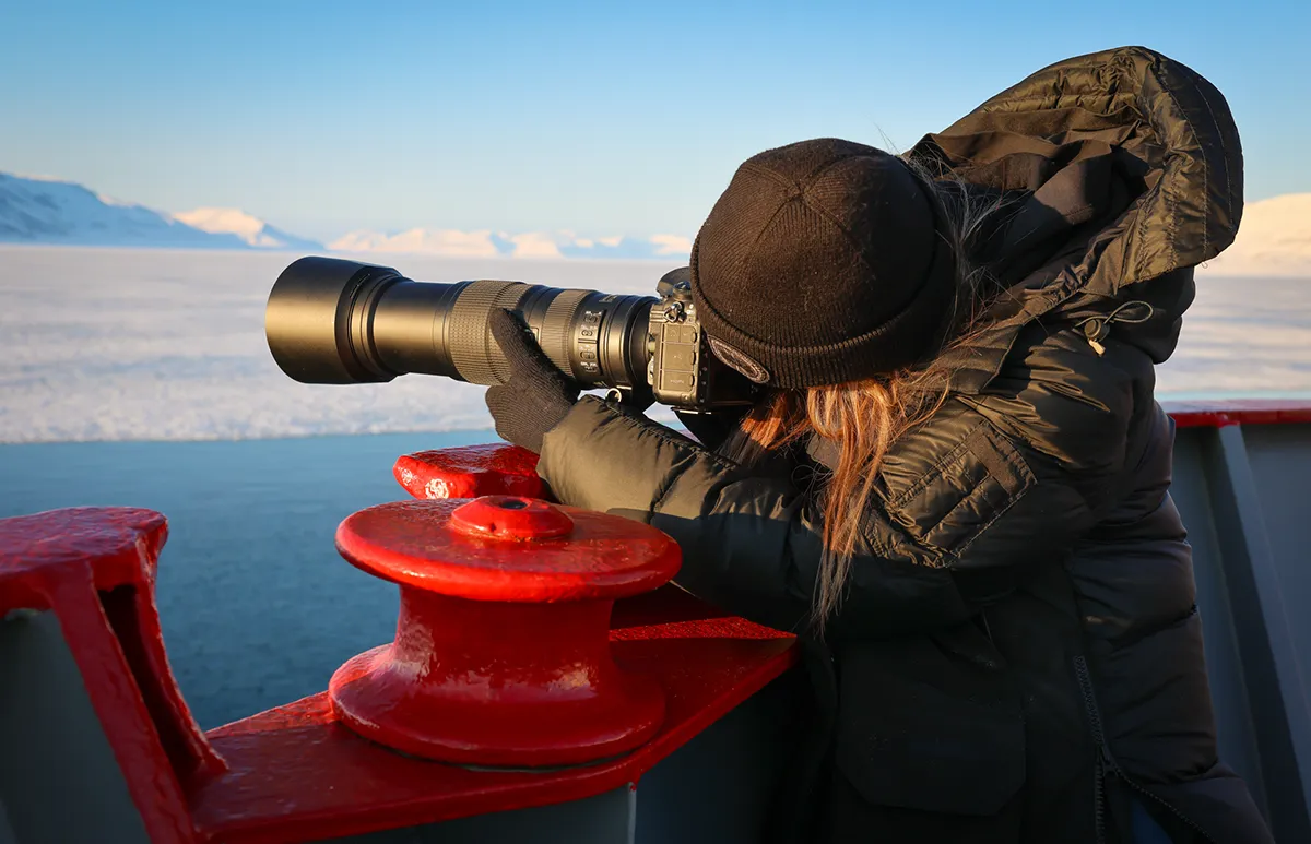 Photographer with telephoto lens shooting Arctic landscape from the deck of Vikingfjord expedition vessel during production charter