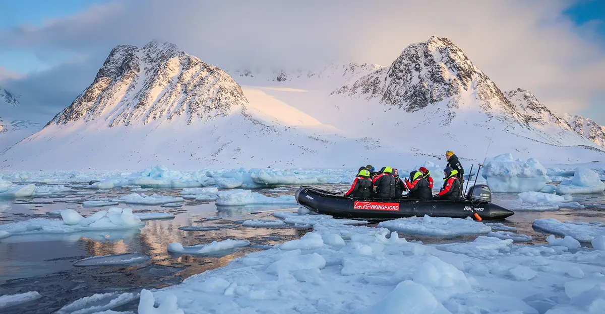 Expedition zodiac with guests navigating ice floes near snowy Svalbard mountains during Vikingfjord cruise